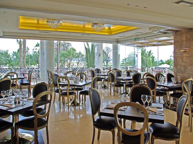 Großes, helles Restaurant mit schwarzen Stühlen, runden Tischen und großen Fenstern zum Garten.