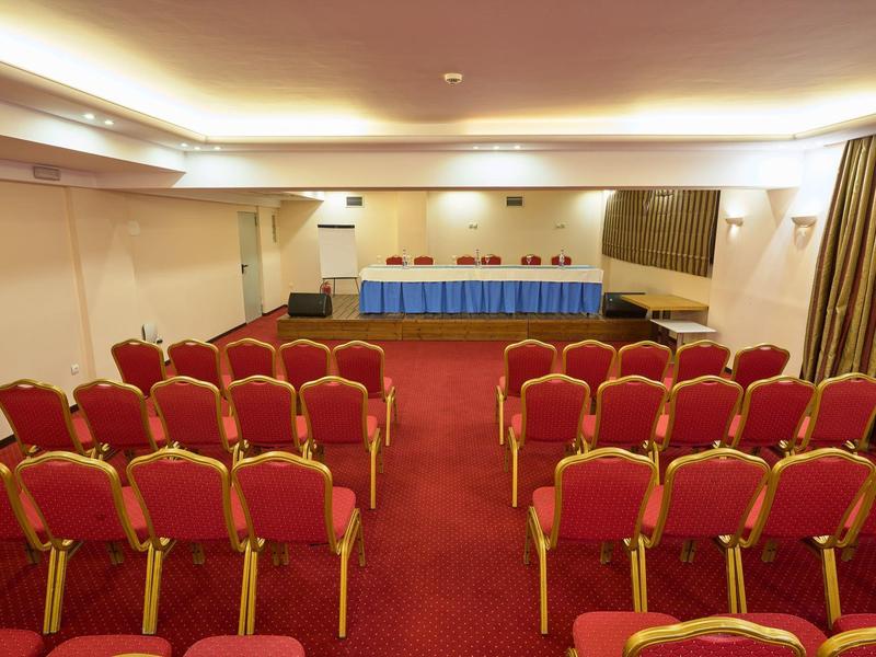 Kleiner Konferenzraum mit roten Stühlen und einem langen Tisch vorne, heller Beleuchtung.