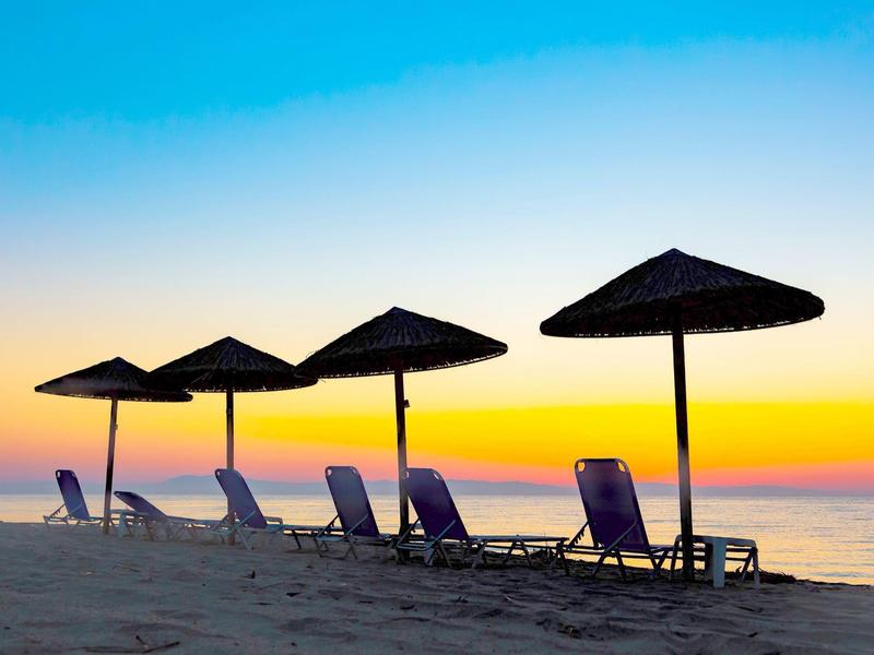 Mehrere Liegestühle mit Sonnenschirmen stehen am Strand bei buntem Sonnenuntergang.