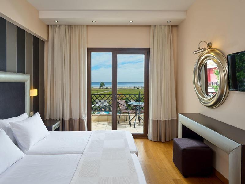 Modernes Schlafzimmer mit Doppelbett, großem Fenster, Balkon und mediterranem Ausblick bei Tageslicht.