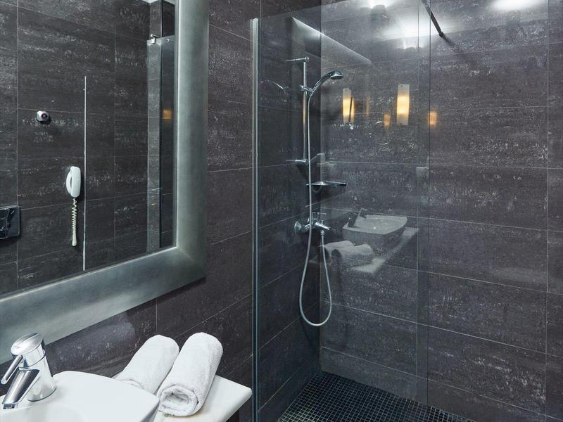 Moderne Dusche mit Glaswand, dunklen Fliesen, Waschbecken und weißen Handtüchern auf Holzregal.