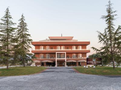 Moderní vícepatrová hotelová budova se dvěma velkými stromy v popředí a dlážděnou cestou.