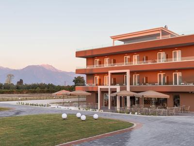 Modernes dreistöckiges Hotel in Orange mit Pool, grünem Rasen und Bergen im Hintergrund bei klarem Himmel.