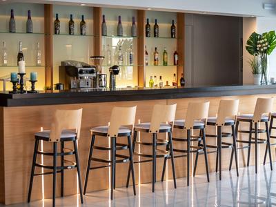 Moderne helle Rezeption mit Holztheke, Pflanze links, und Frau am Telefon im Hintergrund.