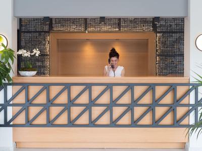 Rezeptionistin spricht am Telefon hinter einer modernen Hotelrezeption mit Pflanzen und Dekor.