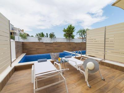 Moderner Balkon mit Holzboden, weißen Stühlen, blauem Sitzpolster und Pflanzen im Hintergrund.