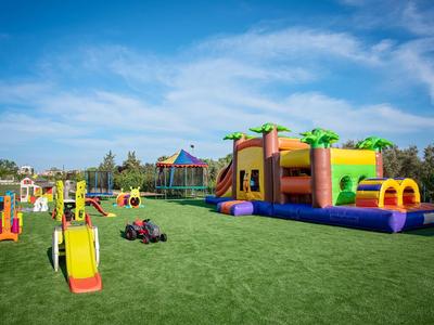 Freizeitpark im Freien mit aufblasbarer Hüpfburg, Klettergeräten und Spielzeugen auf grünem Rasen.