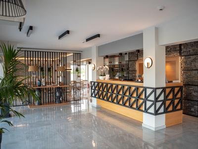 Heller Hotel-Empfang mit weißem Tresen, Holzverkleidung, Pflanzen und moderner Beleuchtung.