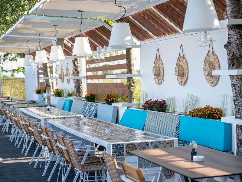 Modernes dreistöckiges Hotel in Orange mit Pool, grünem Rasen und Bergen im Hintergrund bei klarem Himmel.