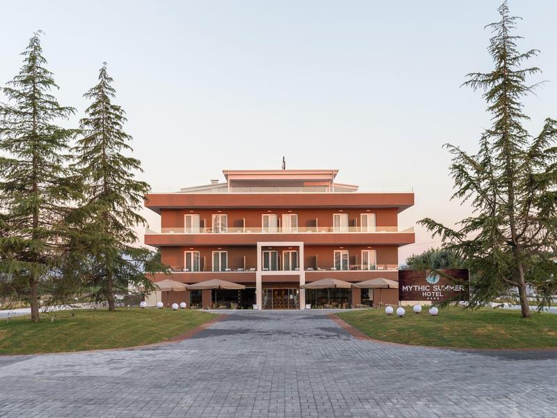 Ein großes, rotes Gebäude mit mehreren Balkonen, umgeben von hohen Bäumen und einem gepflasterten Weg.