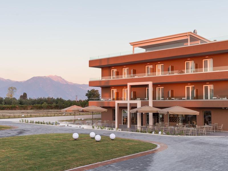 Modernes dreistöckiges Hotel in Orange mit Pool, grünem Rasen und Bergen im Hintergrund bei klarem Himmel.