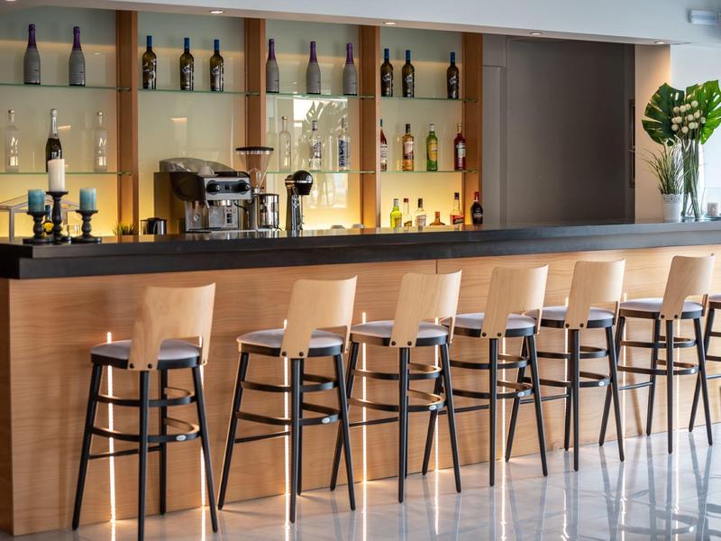 Moderne helle Rezeption mit Holztheke, Pflanze links, und Frau am Telefon im Hintergrund.