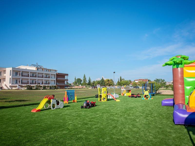 Weitläufige Spielwiese mit bunten Spielgeräten und Hüpfburg unter klarem blauem Himmel.