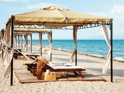 Strandliegen unter einem Sonnenschutz aus Stoff am Sandstrand mit Meer im Hintergrund.