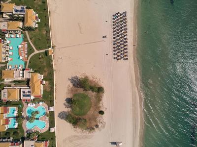 Zdjęcie z powietrza plaży z leżakami, przylegającymi basenami i budynkami obok morza.