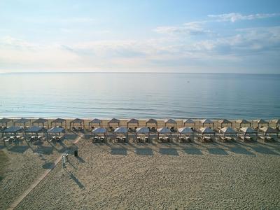 Plaża z rzędami leżaków pod parasolami nad spokojnym morzem.