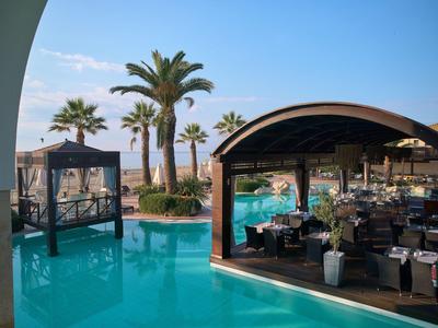 Basen hotelowy z palmami, meblami lounge i widokiem na morze przy czystym niebie.