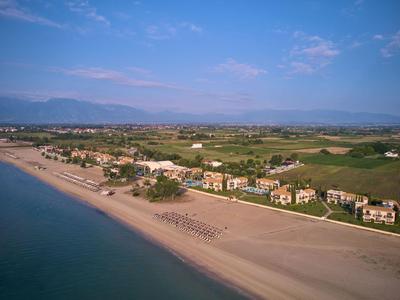 Widok z lotu ptaka na spokojną plażę z hotelami i zielonymi polami w tle.