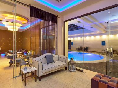 Nowoczesna przestrzeń hotelowa z wygodną sofą i basenem za szklaną ścianą z oświetleniem nastrojowym.