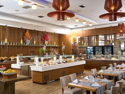 Nowoczesna restauracja z bufetem i elegancko nakrytymi stołami w jasnej, ciepłej atmosferze.