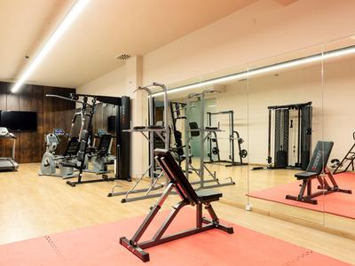 Moderner Fitnessraum mit Trainingsgeräten und großen Spiegeln in hellem Raum.