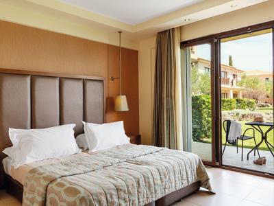 Helles Hotelzimmer mit großem Bett und Terrassentür mit Blick auf einen Garten und Sitzbereich.