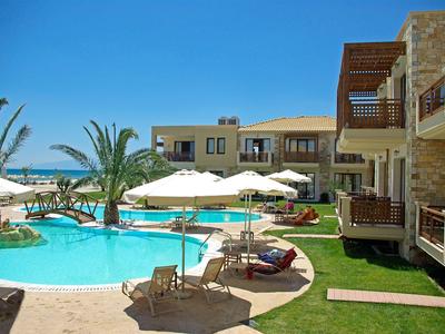 Hotelpool mit Sonnenliegen, Sonnenschirmen und Palmen unter klarem blauem Himmel.