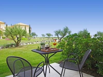 Terrasse mit zwei Stühlen und einem Tisch mit Getränken, Blick auf einen gepflegten Garten mit Olivenbäumen.