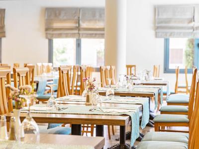 Světla jídelna s dřevěnými židlemi a stoly prostřenými na jídlo, přirozené světlo.