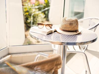 Malý kulatý stůl s kloboukem, slunečními brýlemi a otevřenou knihou v jasném prostředí.