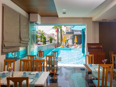 Vnitřní jídelní prostor s dřevěnými židlemi a stoly s výhledem na slunný bazén se slunečníky.