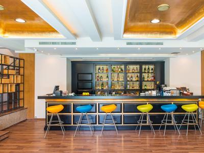 Bar moderno dell'hotel con sgabelli colorati, pavimento in legno e illuminazione calda al soffitto.