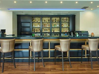 Area bar dell'hotel moderna con sedie chiare e scaffale ben fornito sullo sfondo.