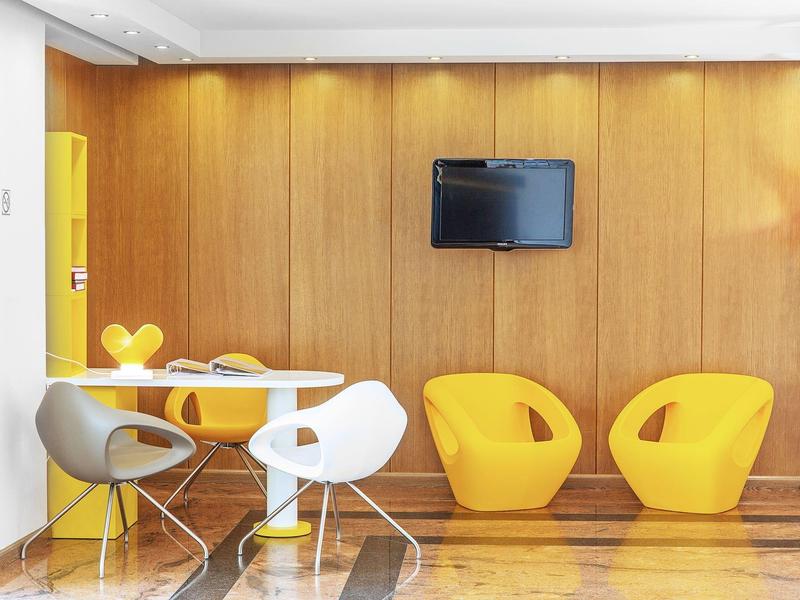 Moderní salón s dřevěnými stěnami, žlutými a bílými židlemi a televizí na stěně.