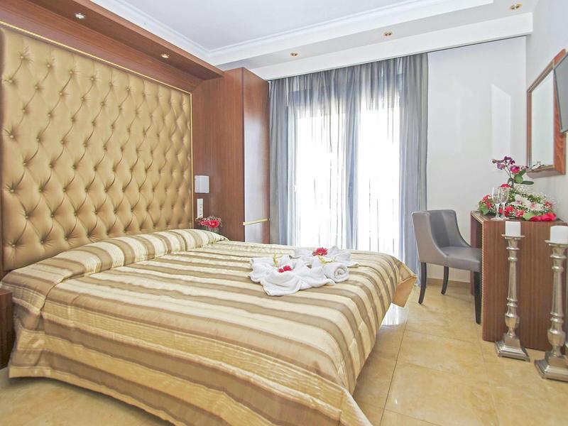 Světly hotelový pokoj s velkým čalouněným čelem postele, pruhovaným povlečením a psacím stolem u okna.