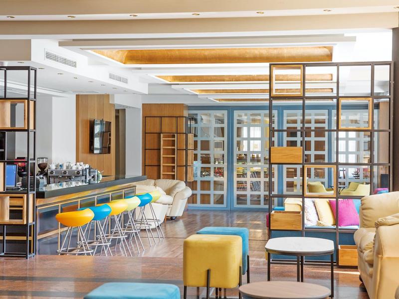 Jasný hotelový salon s barovými židlemi, barevným posezením a moderními dřevěnými prvky.