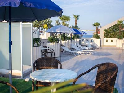 Ein sonniger Außenbereich mit Tischen und Stühlen sowie Liegestühlen und Sonnenschirmen neben einem Pool.