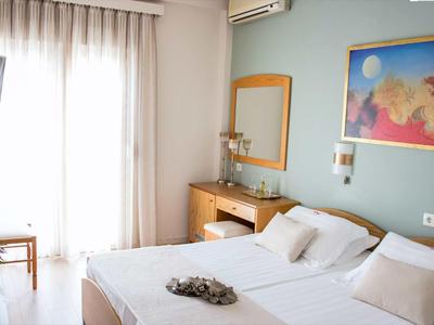 Hell eingerichtetes Hotelzimmer mit Doppelbett, Tisch, Stuhl und einem hellen Vorhang am Fenster.