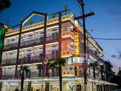 Beleuchtetes Hotelgebäude mit mehreren Etagen und Geschäften bei Dämmerung.