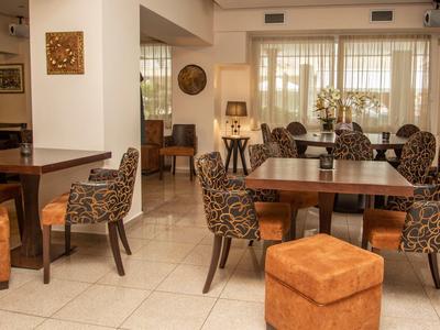 Gemütlicher Hotel-Loungebereich mit Tischen, gepolsterten Stühlen und großen Fenstern.