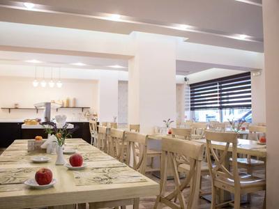 Sala da pranzo luminosa e moderna con tavoli e sedie in legno, apparecchiata con mele e fiori.