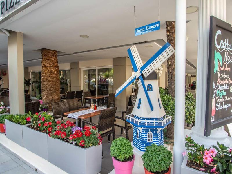 Venkovní posezení hotelu s květináči a dekorativním větrným mlýnem vedle tabule.