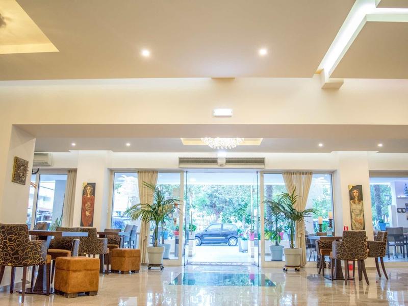 Světlá hotelová lobby s posezením, skleněnou stěnou a výhledem na venkovní rostliny.