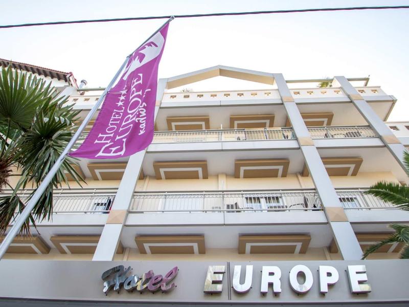 Pohled na fasádu hotelu Europe s balkony a vlajkami v popředí.