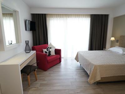 Lichte hotelkamer met tweepersoonsbed, rode fauteuil, bureau en aan de muur gemonteerde tv