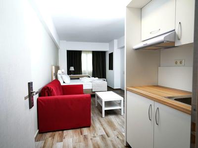 Kleine woonkamer met rode bank, witte salontafel en kitchenette met houten aanrechtblad.