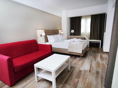 Hotelkamer met tweepersoonsbed, rode bank, witte salontafel en houten vloer