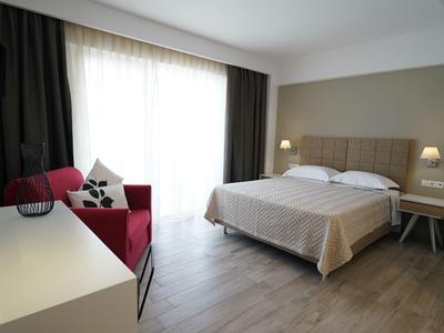 Elegant hotelkamer met groot bed, rode fauteuil en lichte houten vloer.