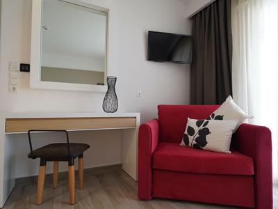 Coin salon confortable avec fauteuil rouge, coussin et bureau dans une chambre d'hôtel lumineuse.