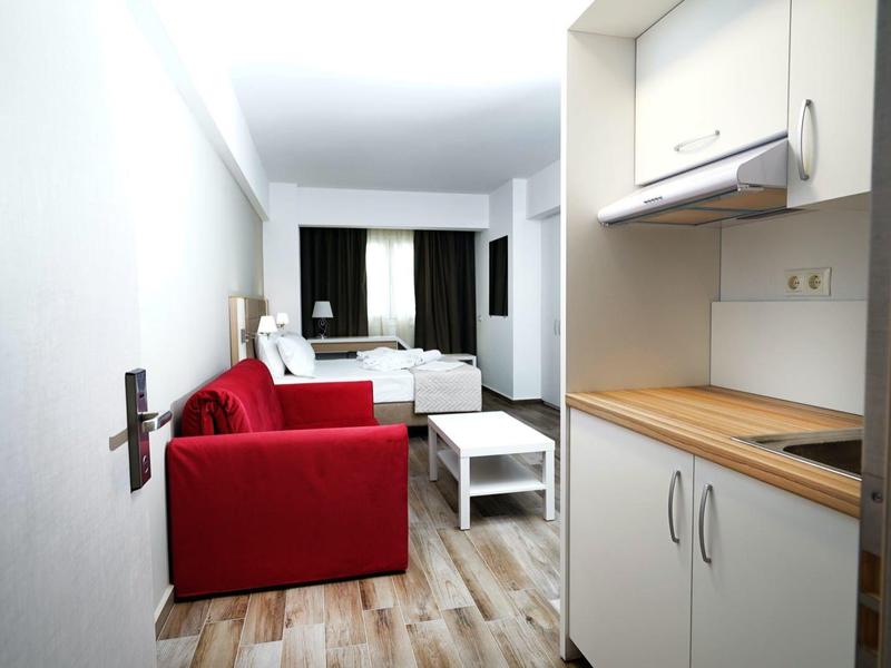 Kleine woonkamer met rode bank, witte salontafel en kitchenette met houten aanrechtblad.